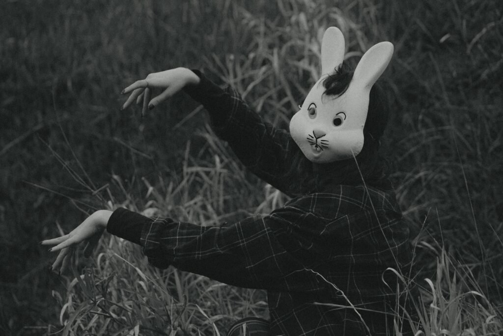 pexels-photo-13662629-13662629 A mysterious figure wearing a rabbit mask poses in tall grass, creating an eerie atmosphere.